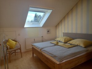 Un dormitorio con tragaluz, una cama con ropa de cama estampada, una silla con cojín amarillo y un radiador.
