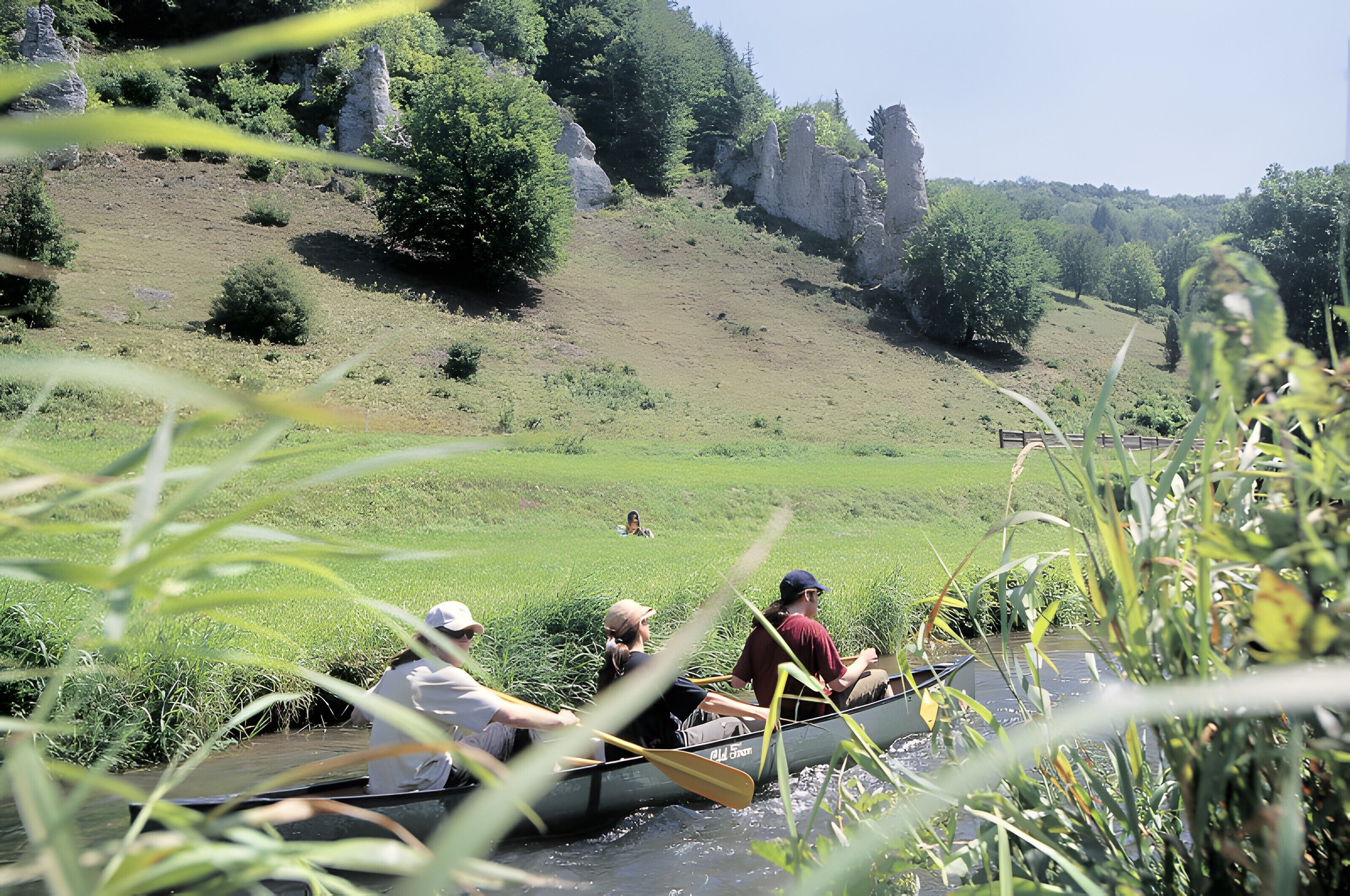 A group of people in a canoe on a river surrounded by greenery and rocky hills.