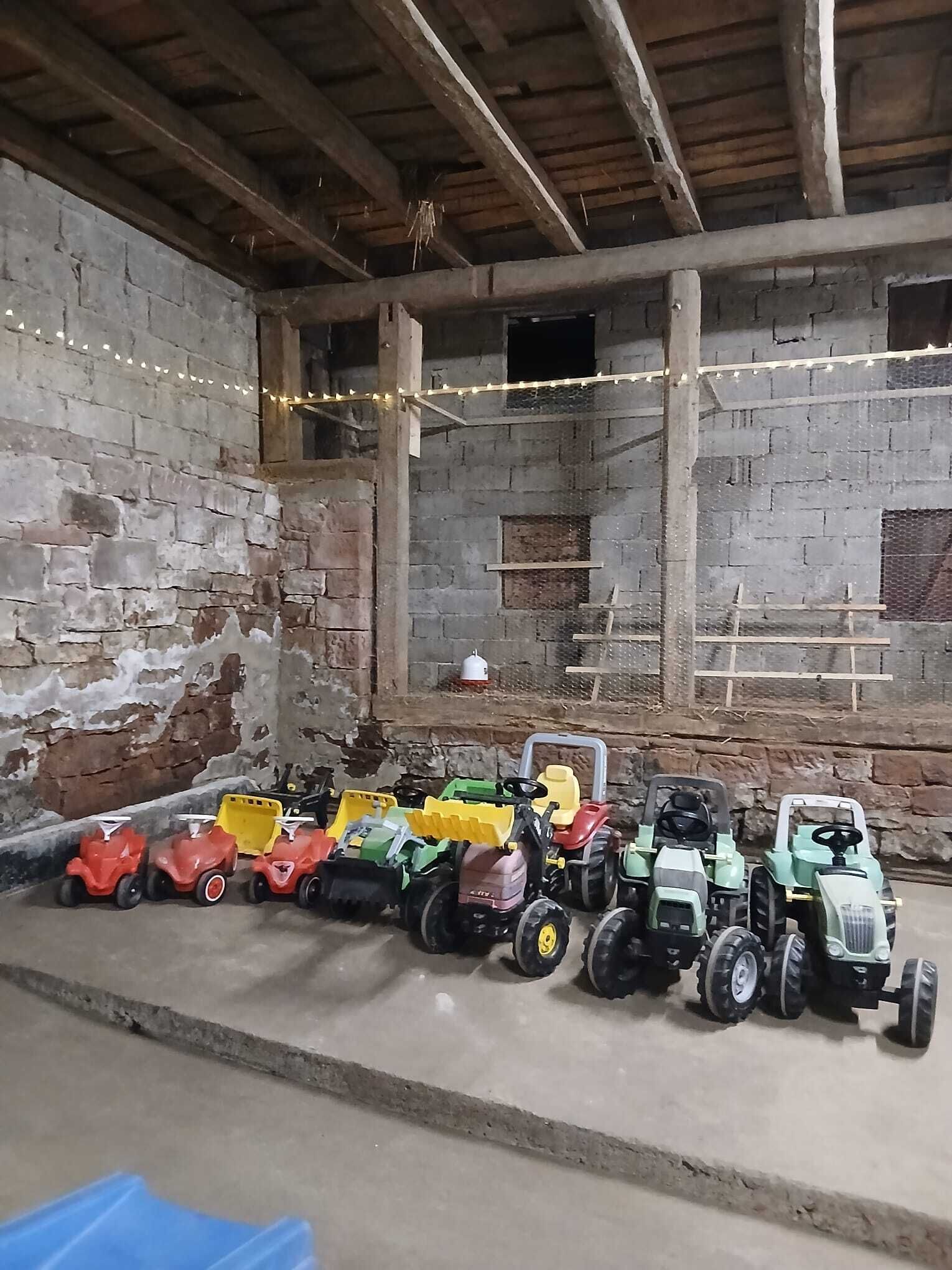 Interno rustico di una stalla con travi in legno e pareti in mattoni, con una fila di colorati trattori giocattolo.