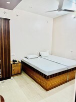 Ein Schlafzimmer mit einem hölzernen Bettgestell, zwei weißen Matratzen, einer kleinen Holzkommode und einem Deckenventilator.