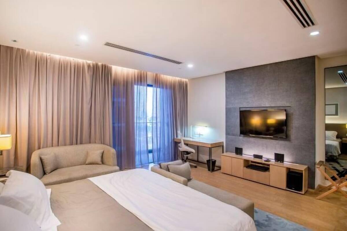 Een hotelkamer met een groot bed, een bureau met stoel, een televisie en een raam met gordijnen.