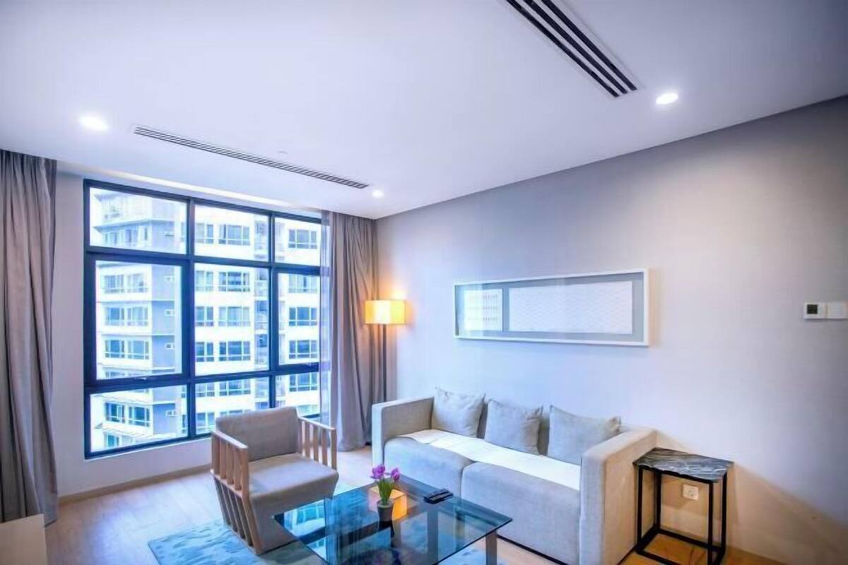 Een moderne hotelkamer met een groot raam, een bank, een glazen salontafel en een klein bijzettafeltje.