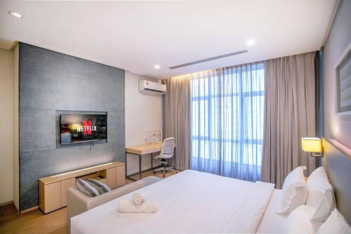 Hotelkamer met een bed, bureau, stoel, een aan de muur bevestigde televisie en een raam met gordijnen.