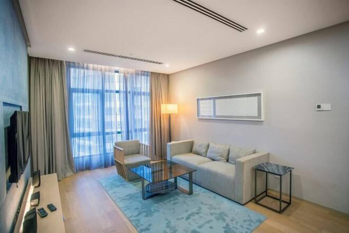 Een moderne hotelkamer met een bank, fauteuil, glazen salontafel en een televisie.