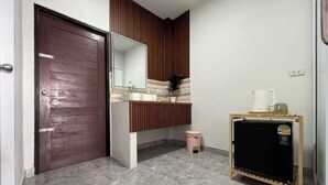A bathroom with a wooden door, a mirror, a sink, a toilet, and a small cabinet. - Wilawan home (Koh Samui)
