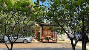A small, modern building with a wooden deck and a signboard, surrounded by lush greenery and parked cars. - Wilawan home (Koh Samui)