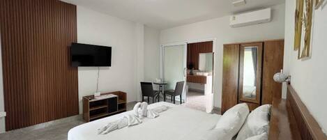 Habitación de hotel moderna con una cama grande, un televisor de pantalla plana en la pared, un escritorio con sillas y un armario.