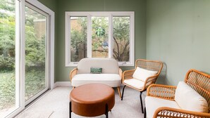 Une pièce dotée d'une grande fenêtre, d'un canapé blanc, de fauteuils en osier et d'un pouf rond.