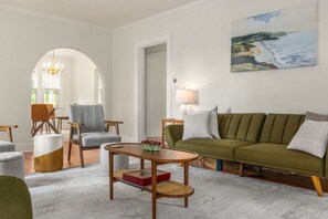 Een woonkamer met een groene bank, een houten salontafel en een stoel met een grijze kussens.