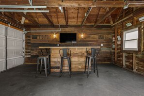 Un espace bar avec un mur en bois, un téléviseur à écran plat et trois tabourets de bar.