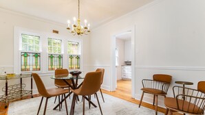 Un coin repas avec une table ronde, des chaises marron, un lustre et des vitraux.