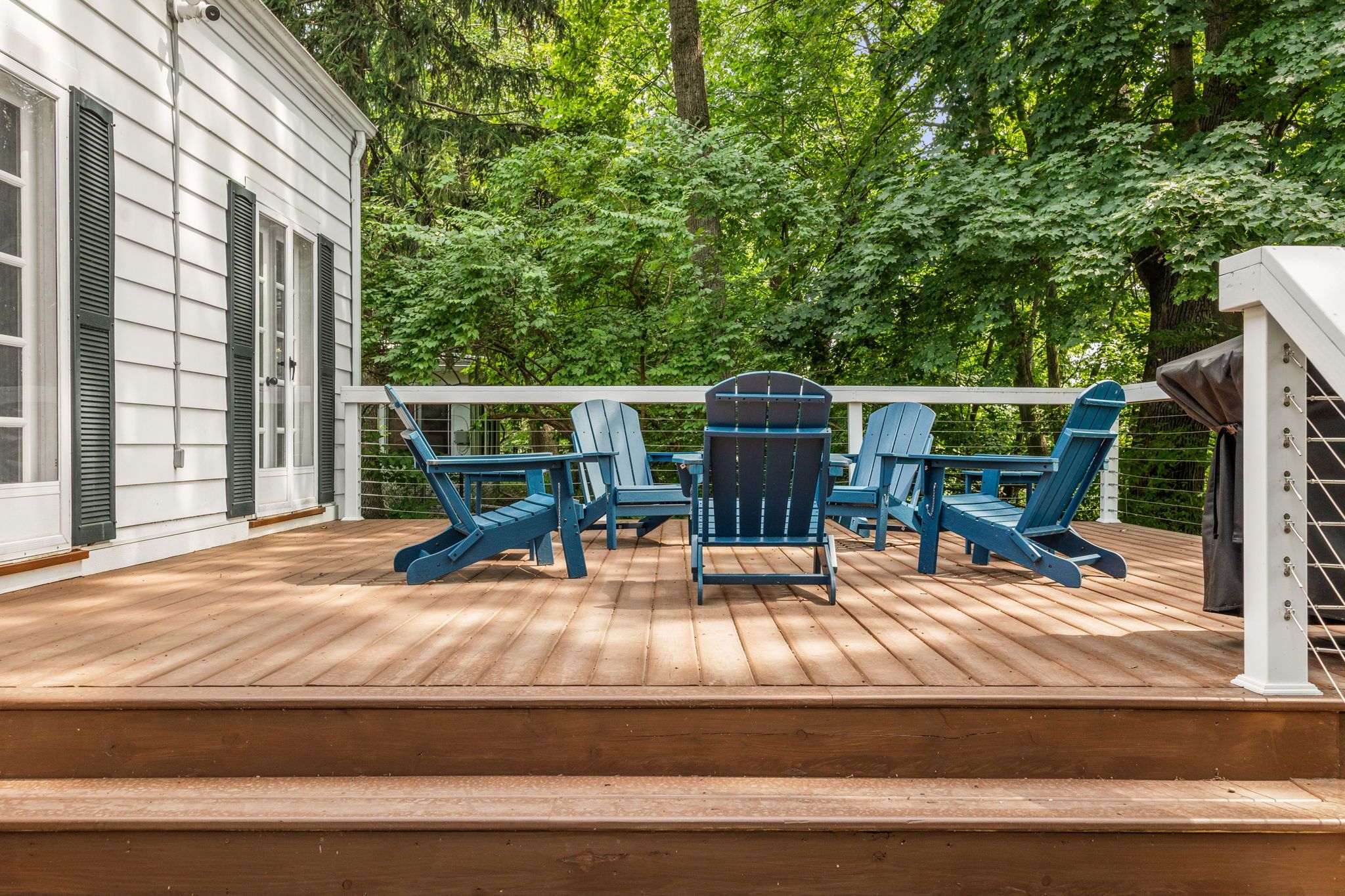 Um deck de madeira com cadeiras Adirondack azuis e um corrimão branco.