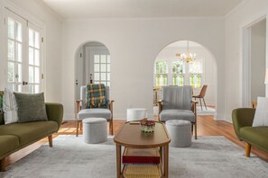 Un salon spacieux comprenant un canapé, des fauteuils, une table basse et un coin repas agrémenté d’un lustre.
