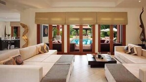 A spacious living room with a large sofa set, a coffee table, and a view of an outdoor pool area through a glass door. - Laguna Waters - Lake View Villa, 5 Bedrooms (Bang Tao)