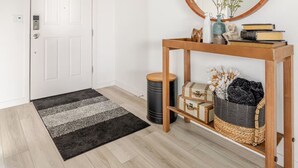 A hallway with a wooden console table, a mirror, a door, and a black and white striped rug.