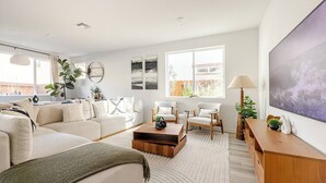 A modern living room with a sectional sofa, two armchairs, a coffee table, and a large painting on the wall.