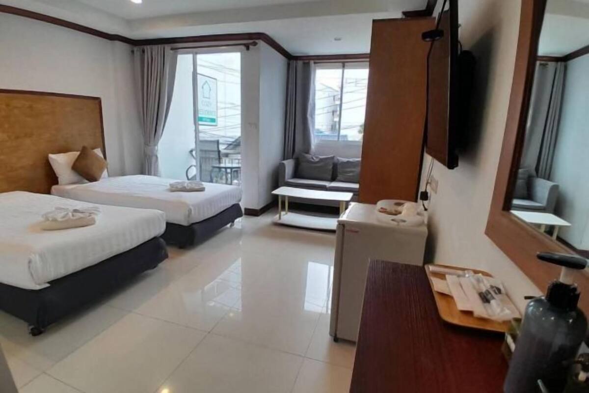 A hotel room with two beds, a sofa, a small table, a TV, and a window with curtains.