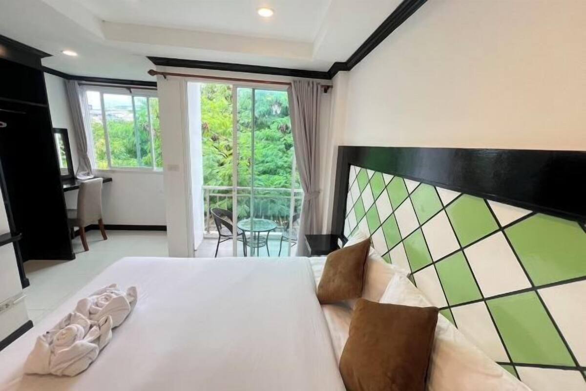 A hotel room with a bed, a desk, a chair, and a balcony with a view of greenery.