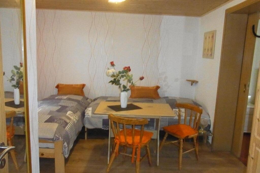 A small, cozy room with two single beds, a wooden table, and two chairs.