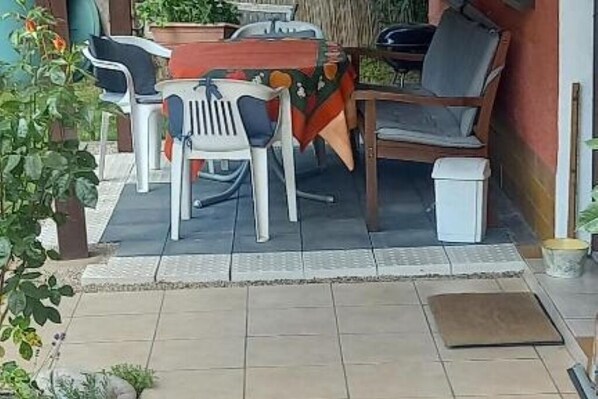 Een buitenruimte met plastic stoelen en een tafel, omringd door planten en een betegelde vloer.