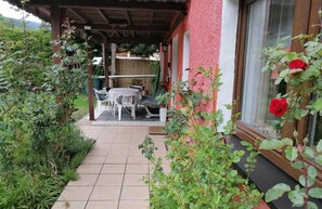 Un patio cubierto con una mesa y sillas, rodeado de follaje y una pared roja.