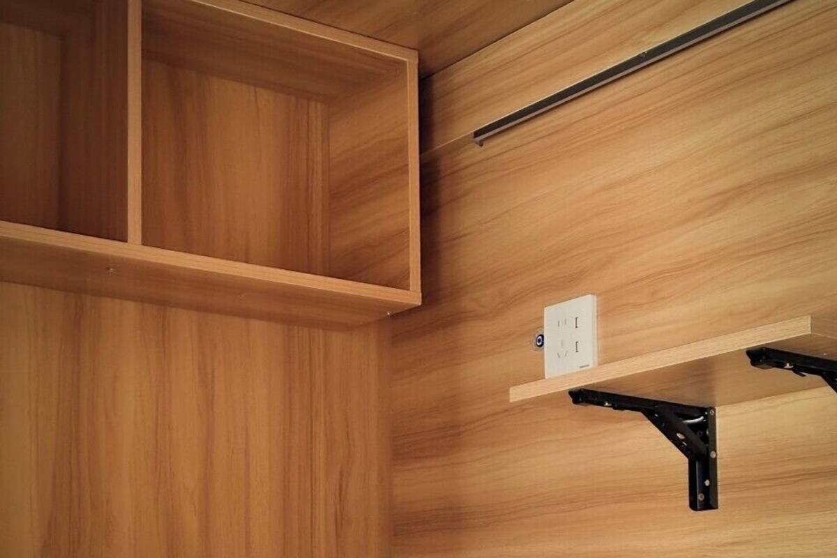Una cama litera con panel de madera, un estante con toma de corriente y un escritorio extraíble.