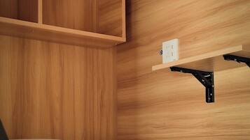 A bunk bed with a wooden wall, a shelf with a power outlet, and a pull-out desk.
