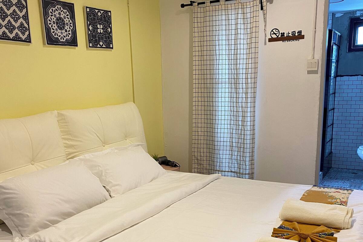 Una cama bien hecha con sábanas blancas, un cartel de no fumar y decoración de pared.