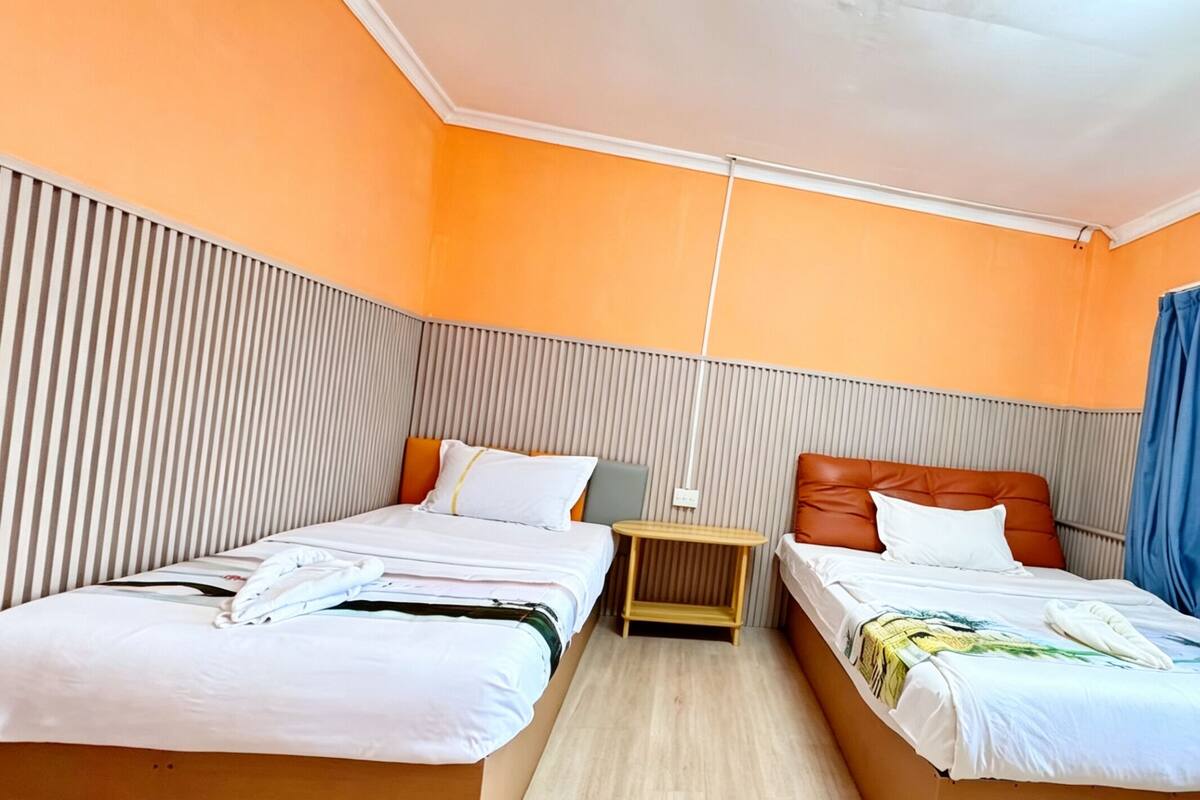 Habitación de hotel con dos camas, una mesita, un equipo de aire acondicionado y una ventana con cortinas.