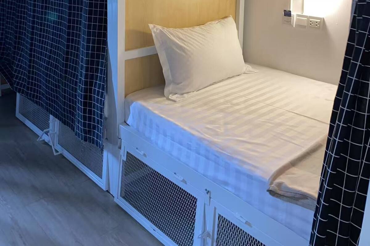 Una cama litera con cabecera, una lámpara de noche y una puerta marcada con la letra 'G'.