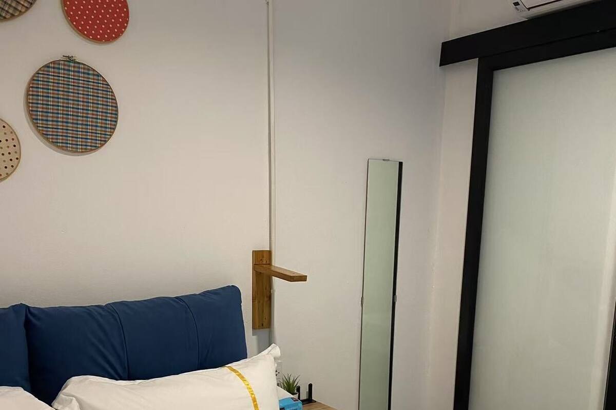 Una habitación de hotel con cama, mesita de noche de madera, espejo y puerta corredera.