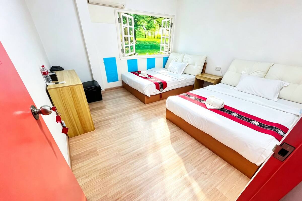 Habitación de hotel con dos camas, un escritorio, una silla, un ventanal con vistas a zonas verdes y una puerta roja.