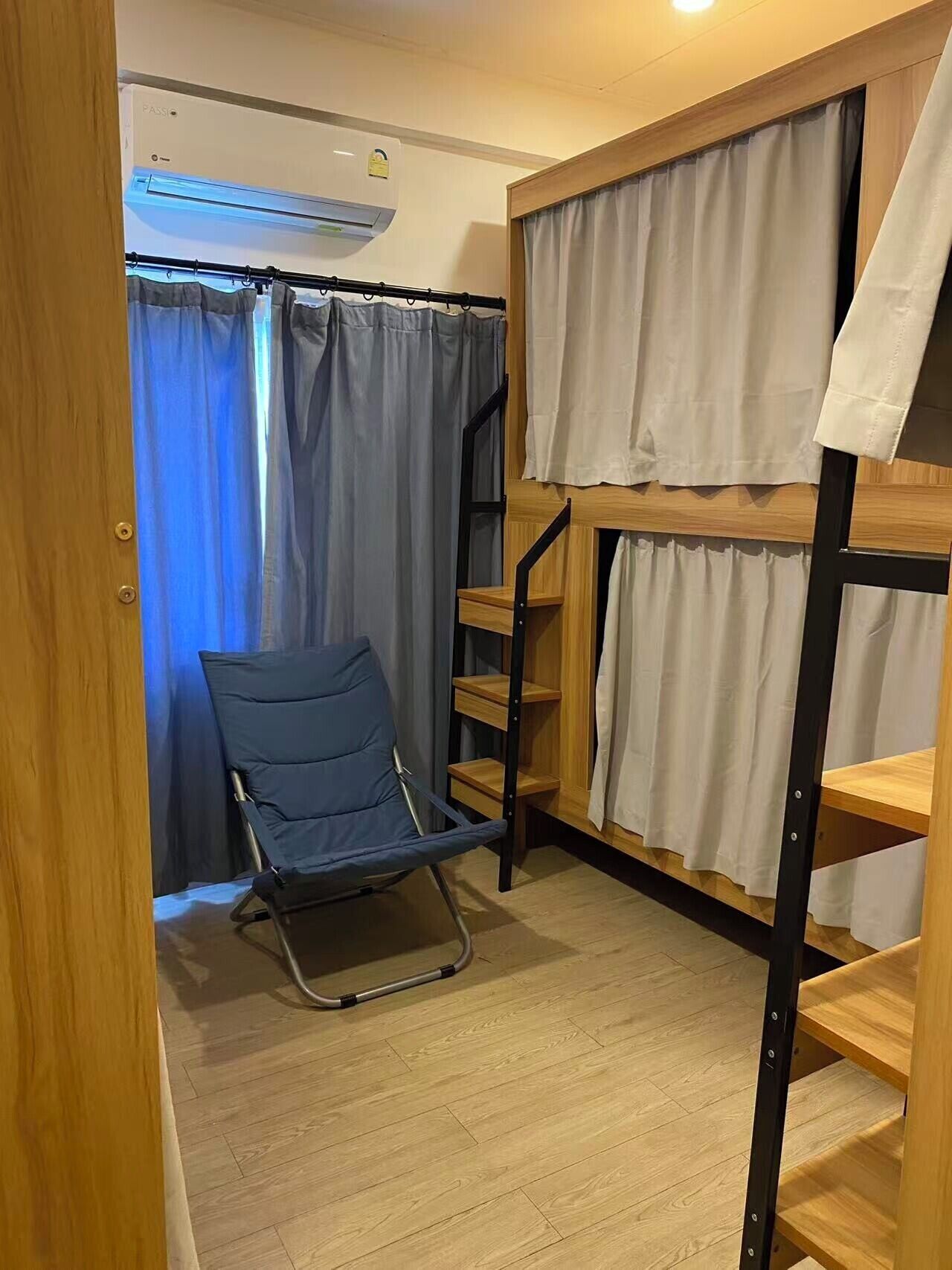 Una cama litera con escalera de madera, una silla azul y una cortina.