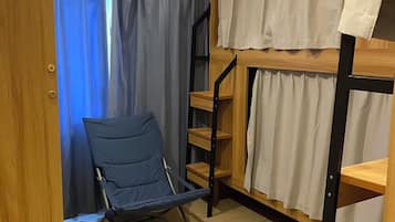 Una cama litera con escalera de madera, una silla azul y una cortina.