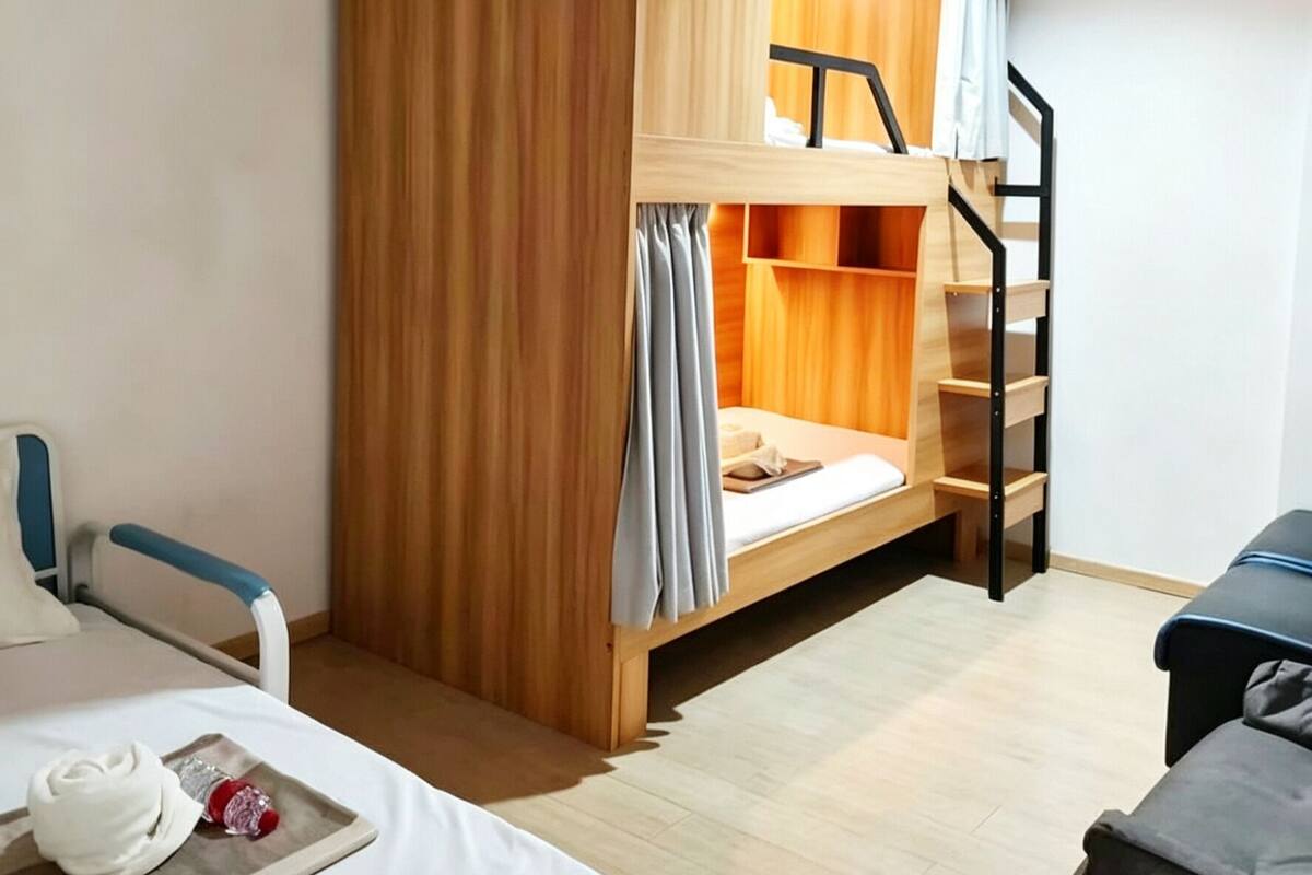 Una cama litera con acabados de madera, un escritorio pequeño con una silla y una mesita de noche con un revistero.