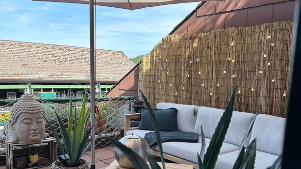 Eine Terrasse mit einer Couch, einer Buddha-Statue und Topfpflanzen.