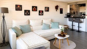 Ein modernes Wohnzimmer mit einem weißen Sofa, einem Couchtisch und einer Küchenzeile im Hintergrund.