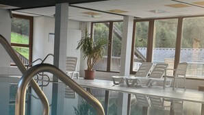 Ein Hallenbad mit Metallhandlauf, Liegestühlen und einem Topfpflanzen.