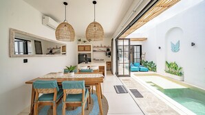 A modern kitchen with a dining area, a small pool, and a living space with a large window. - Villa Lumière 1 Seminyak (Seminyak)