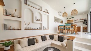 A modern living room with a sectional sofa, a dining area with a wooden table and chairs, and built-in shelves with decorative items. - Villa Lumière 1 Seminyak (Seminyak)