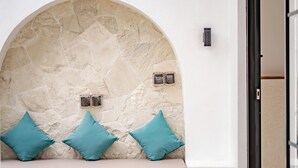 A stone bench with teal cushions, a stone wall, and a door to a room. - Villa Lumière 1 Seminyak (Seminyak)