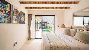 A modern bedroom with a large bed, a sliding glass door leading to a pool area, and colorful artwork on the wall. - Villa Lumière 1 Seminyak (Seminyak)