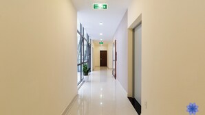 A clean, well-lit hotel corridor with a clear exit sign, a potted plant, and a door at the end.