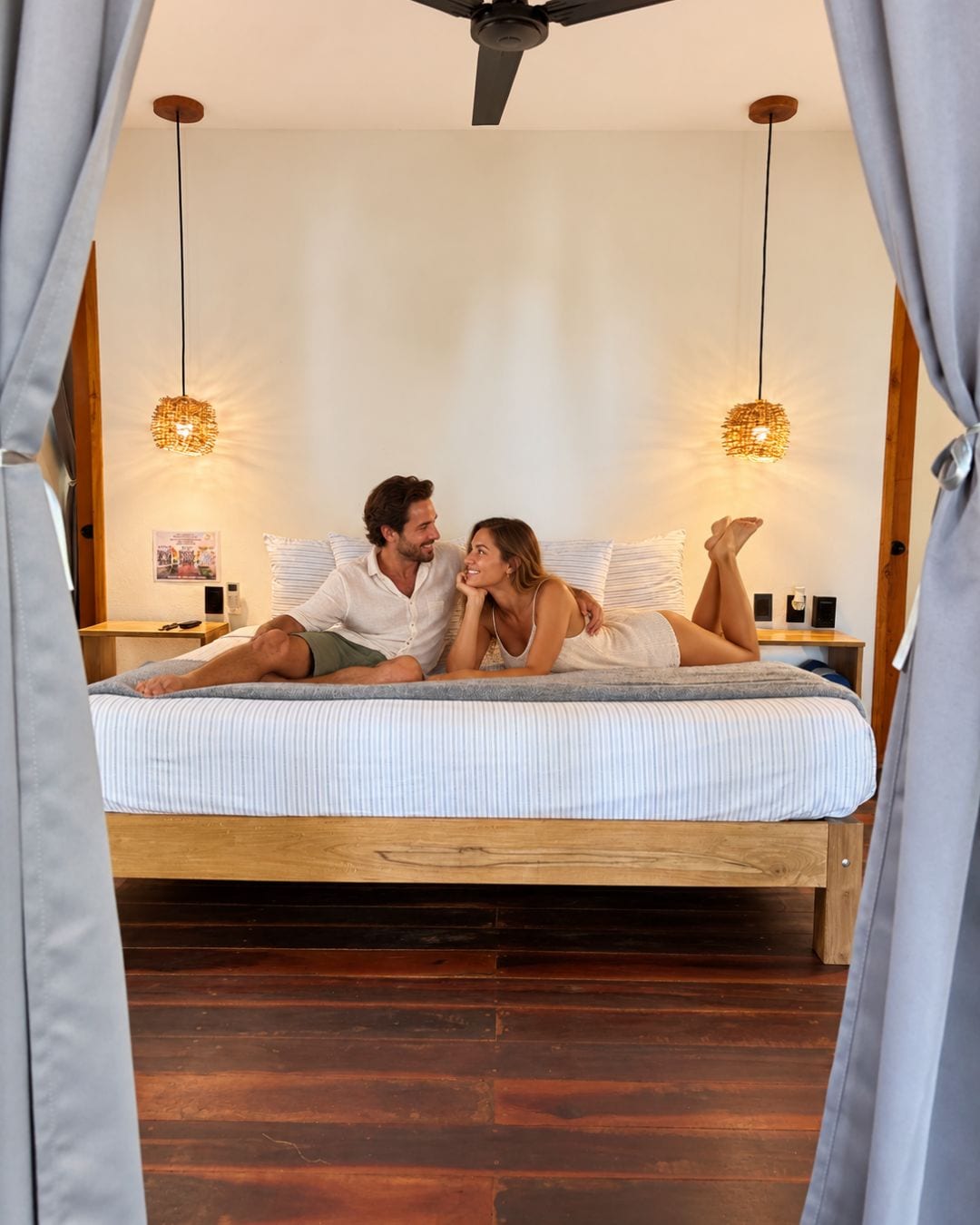 A bed with a wooden frame, two hanging lamps, and a poster on the wall.