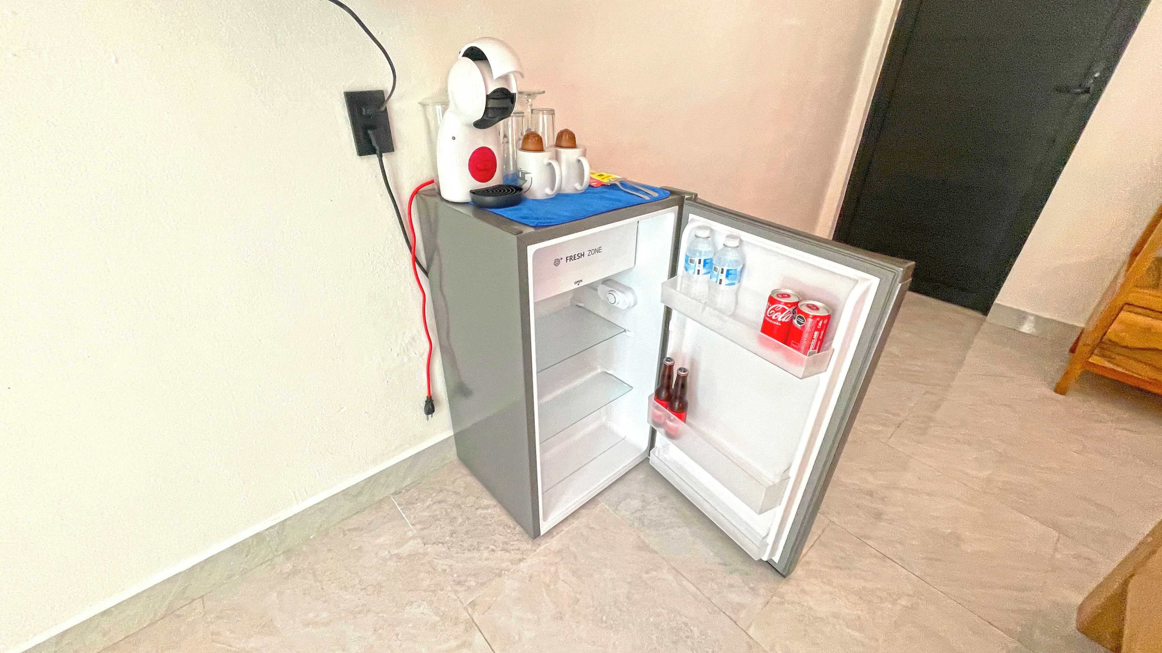 A compact refrigerator with a fresh zone label, a coffee maker, and a few bottles and cans.