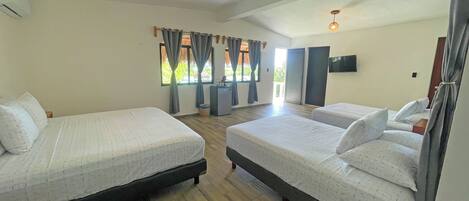 A hotel room with two beds, a TV, a small refrigerator, and a window with curtains.