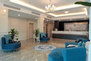 A hotel lobby with a reception desk, two blue armchairs, and a chandelier. - The Host Hotel (Ipoh)