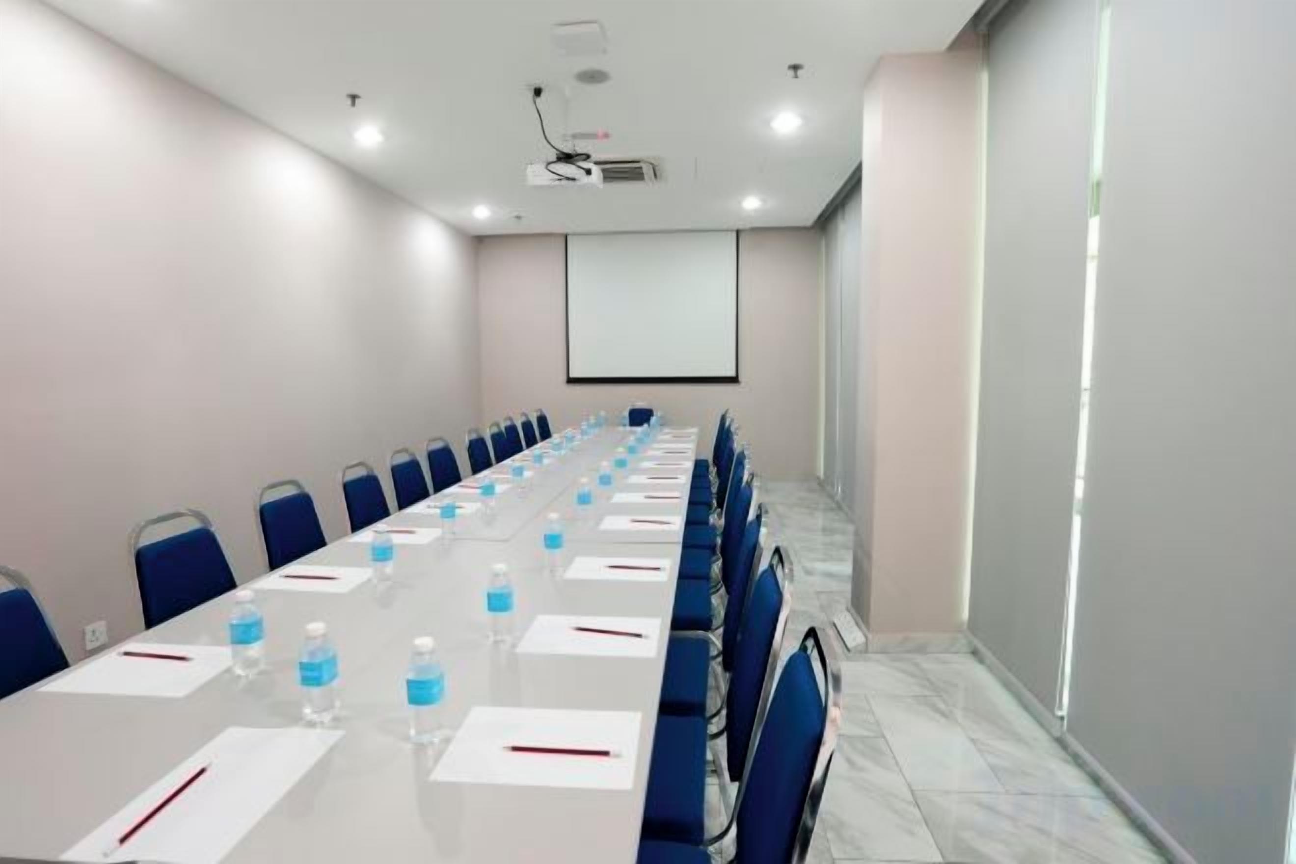 A conference room with a long table, chairs, water bottles, and a projector screen.