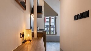 Un couloir avec un banc en bois, un luminaire fixé au mur et une fenêtre donnant sur des immeubles.