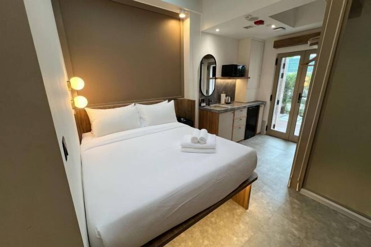 A hotel room with a bed, bedside lamps, a small desk with a mirror, and a view of the outside.